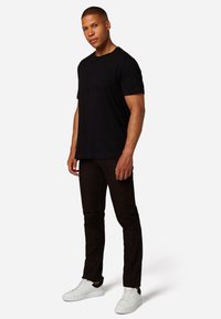 Zwarte katoenen t-shirt, gecombineerd met donkerbruine slim-fit broek en witte sneakers met zwarte accenten. Eenvoudig ontwerp, geen patronen of logo's.