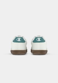 Hvite sneakers med teal-aksenter og logo bak, gummisåle og glatt tekstur. Minimalistisk design uten synlige logoer på siden.