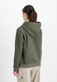 Olive zeleno pulover s prostorno kapuco, ribanim manšetama in robom, izdelan iz gladkega materiala iz bombažne mešanice. Zadaj ni grafike.