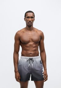 Γκρι βερμούδα για κολύμπι με σχεδιασμό διαβάθμισης, ελαστική μέση, κορδόνι ρύθμισης και εκτύπωση λογοτύπου στο πλάι. Λείο, ελαφρύ ύφασμα.