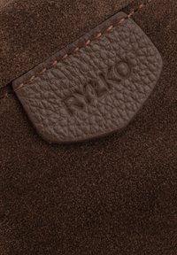 Brązowa skórzana łatka z wytłoczonym logo "RYŁKO", przyszyta do teksturowanego brązowego zamszu, z gładkim brzegiem i bogatym, głębokim kolorem.
