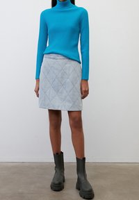 Turquoise geribbelde coltrui gecombineerd met een lichtblauw doorgestikt minirokje en zwarte enkellaarsjes met dikke zolen.