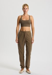 Brauner sportlicher Crop-Top und passende lockere Jogginghosen mit elastischem Bund. Texturierte Schuhe mit offener Webart und runder Zehenpartie.