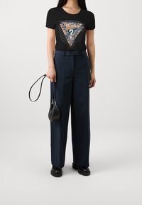 Svart kortärmad T-shirt med triangelgrafik och nitar, kombinerad med högmidjade navy vida byxor och svarta ankelskor.