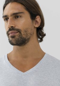 T-shirt grigio con scollatura a V in un morbido tessuto leggero. Presenta una texture sottile e un colletto pulito, evidenziando un design semplice e moderno.
