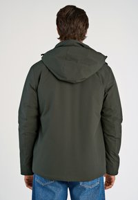 Tummanvihreä parka-takki hupulla, jossa on sileä pinta ja virtaviivainen muotoilu. Takana näkyy siistit linjat ja vähäinen yksityiskohtaisuus.