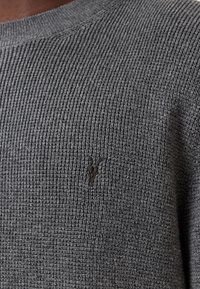 Szary sweter dziany z teksturowanym wzorem, okrągłym dekoltem i małym haftowanym logo w ciemnoszarym kolorze na klatce piersiowej.