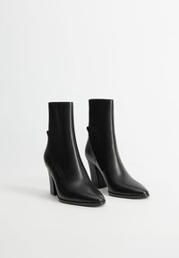 Bottes noires à cheville avec un bout pointu, tige en tissu extensible, et un talon épais. Texture en cuir lisse sans motifs ni accents visibles.