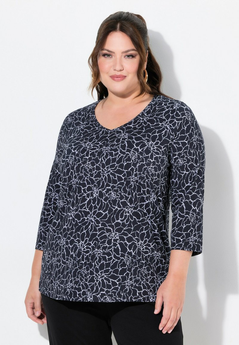 Marineblaue V-Ausschnitt-Bluse mit weißem Blumenmuster, 3/4-Ärmeln und einem lockeren Schnitt. Weicher Stoff mit glatter Textur. Zusammen getragen mit schwarzen Hosen.