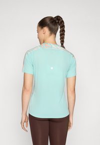 Camiseta deportiva de color azul claro con mangas cortas, que presenta un sutil patrón floral en los hombros. Textura suave, diseño ceñido.