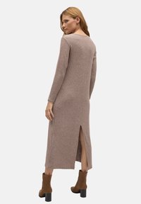 Vestido de punto color topo con mangas largas, textura acanalada, abertura lateral y escote redondo. Combinado con botas de tobillo marrones y un fondo sólido.