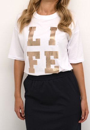 Kvinde iført en hvid T-shirt med store metalliske gyldne bogstaver, der staver "LIFE", kombineret med en sort nederdel.