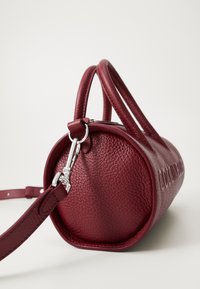 Red textured leather handbag with a cylindrical shape, smooth round base, two handles, and detachable shoulder strap featuring silver hardware.