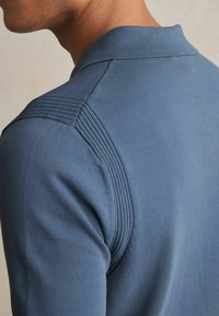 Polo pentru bărbați de culoare albastră, cu un design texturat cu dungi pe umeri și un guler clasic. Material neted, croi ajustat.