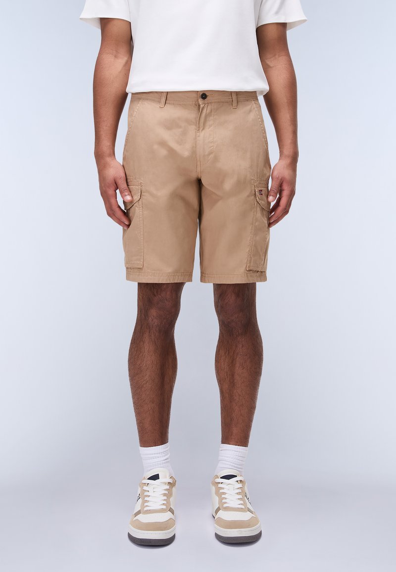 Shorts cargo beige confeccionados en una mezcla de algodón con bolsillos laterales, corte regular, cierre de botón y una textura suave, combinados con zapatillas beige.