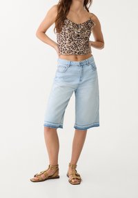 Oříznutý béžový top s leopardím potiskem a volánkovým výstřihem; světle modré bermudy z denimu; hnědé sandály na řemínky s přezkami a plochou podrážkou.