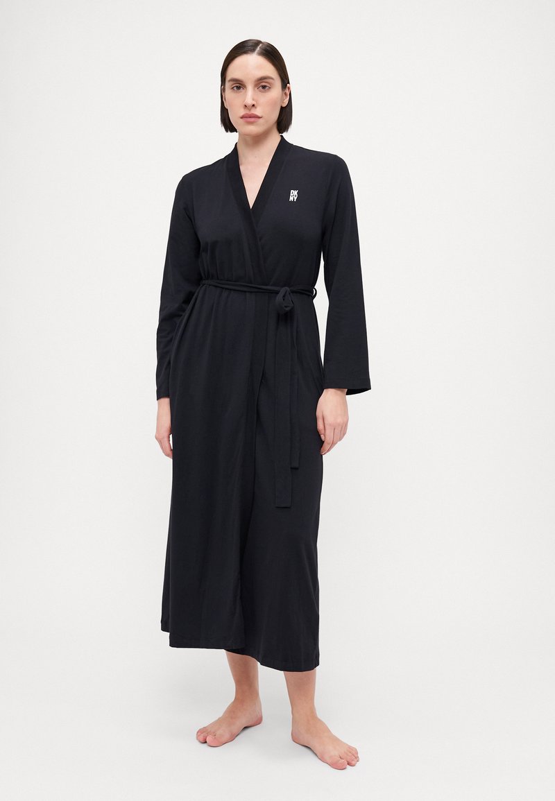 Robe noire à manches longues en tissu doux, avec un design enveloppant, une ceinture à nouer et un petit logo sur la poitrine. Texture lisse.