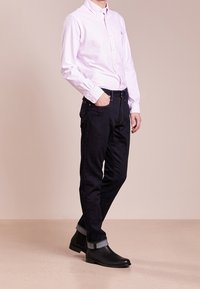 Ljusrosa randig skjorta med knappar, mörkblå jeans med uppvikta benslut och svarta ankelstövlar. Slät textur, figurnära design med krage.