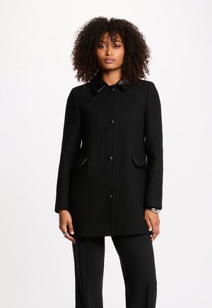 Sort frakke med struktureret stof, rund krave med læderdetaljer, forlommer og knaplukning. Slim fit og lange ærmer.