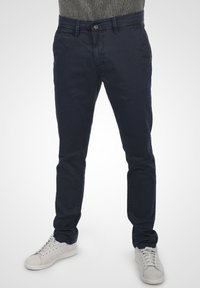 Marineblauwe katoenen chinos met een slim fit, voorzien van een knoopsluiting en zijzakken, gecombineerd met lichtgrijze sneakers.