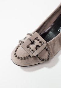 Scarpa piatta in suede grigia con punta rotonda, accentata da una fibbia oversize e borchie circolari disposte lungo la parte superiore e i lati.