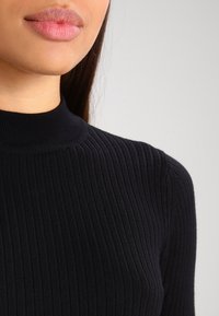 Black ribbed knit turtleneck sweater featuring a fitted design, high neckline, and a smooth texture, ideal for layering in cooler weather.