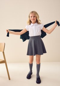 Grauer Rock, weiße Bluse mit Kragen, knielange graue Socken und schwarze polierte Schuhe; grüner Pullover lässig über die Schultern gelegt. Einfaches Design, lässiger Stil.