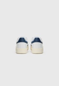 Vita lädersneakers med marinblå accenter, platt gummisula, vadderad krage och slät yta, sedd bakifrån.