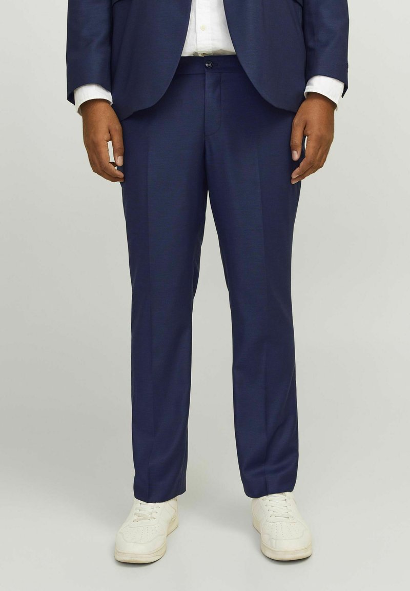 Pantalon de costume bleu marine ajusté avec une finition texturée, doté d'une taille à fermeture à bouton et de jambes droites. Associé à des baskets blanches.