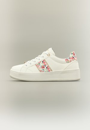 Hvit platåsneaker med snøring, med blomstermønster på hælen og sideststripen på en ensfarget bakgrunn.