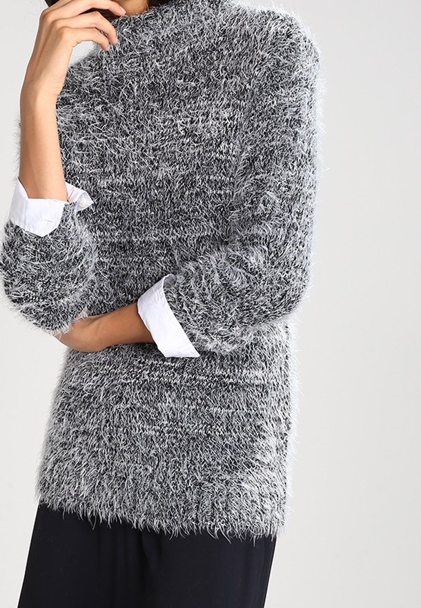 Maglione grigio e bianco fluffy con texture, colletto alto e maniche a tre quarti, indossato sopra una camicia bianca con colletto.