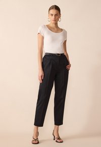 White short-sleeve top paired with high-waisted black trousers. Trousers feature a smooth texture, pleats, and slender silhouette. Black heeled sandals.