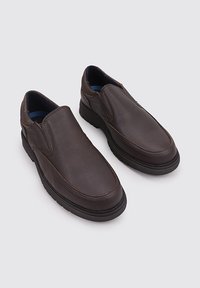 Zapatos de cuero marrón tipo slip-on con punta redonda, cuello acolchado y superficie texturizada. Cuentan con una suela de goma para un mejor agarre y comodidad.