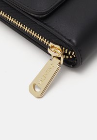 Czarny skórzany portfel z złotym zamkiem i elementami. Posiada teksturowaną powierzchnię oraz oznakowany uchwyt zamka. Kompaktowy design.