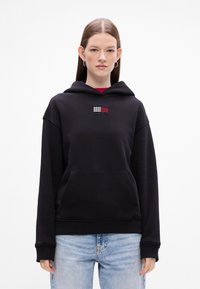 Czarna bluza z kapturem z kieszenią z przodu, z wielokolorowym logo wykończonym cyrkoniami na klatce piersiowej. Miękka tkanina, luźny krój i długie rękawy.