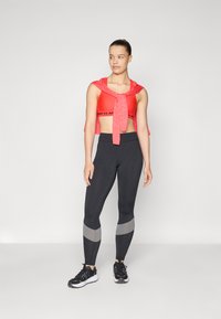Rød sports-bh med snøring foran, svarte leggings med grå detaljer og svarte joggesko. Glatt stoff og tettsittende design.