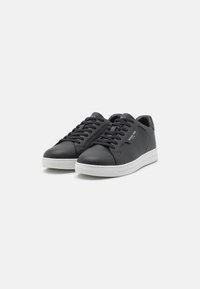 Black leather sneakers with white rubber soles, round toe, and six eyelet lace-up front. Features a logo detail on the side. Smooth texture.