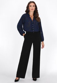Sötétkék áttetsző blúz gombos elejjel és megkötős résszel, magas derekú fekete bő szárú nadrággal és fekete hegyes orrú magassarkúval párosítva.