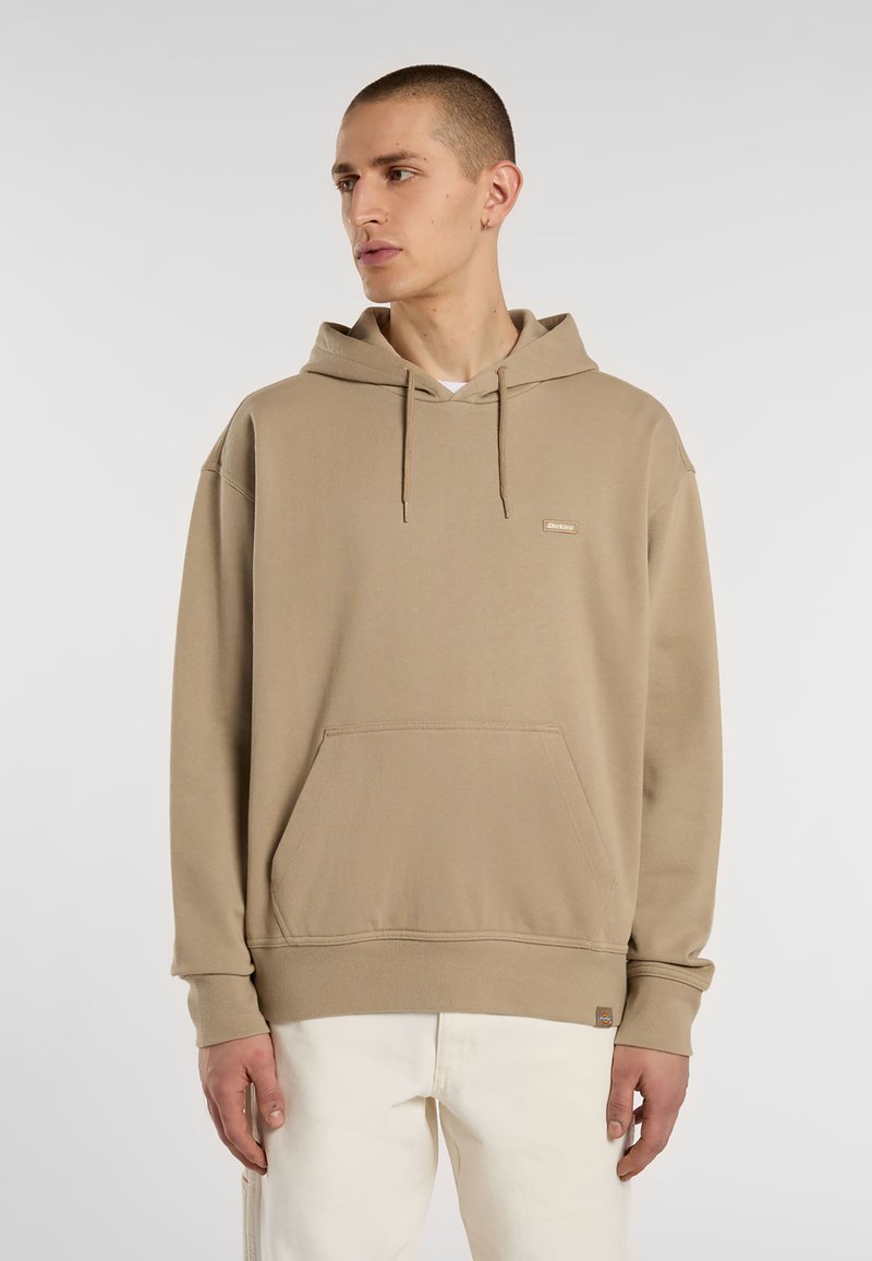 Felpa con cappuccio beige in cotone, dotata di tasca frontale, cordini e una piccola patch con il logo sul petto. Polsini e orlo a costine.