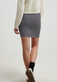 Valko-mustaraidallinen minihame joustavasta kankaasta, yhdistettynä tekstuuroituun kermaiseen neulepuseroon ja rentoihin jalkineisiin.