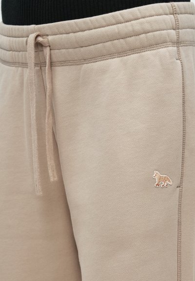 Bežové teplákové nohavice s textúrovaným povrchom, elastickým pásom a šnúrkou. Obsahujú malé hnedé vyšívané loga zvieraťa na nohe.