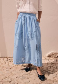 Gonna azzurro chiaro in cotone con cintura elastica, decorata con motivi paisley ricamati e tasche laterali; dettaglio con spacco sul davanti.