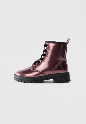 Lśniąca metaliczna fioletowa botka z sznurówkami, z czarną podeszwą i pętelką na pięcie, wyeksponowana na jednolitym jasnym tle.