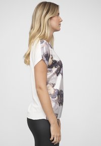 Kortermet topp med flytende design, hvit kropp og lilla-gull marmorert mønster på den ene siden. Mykt stoff med en avslappet passform.