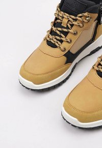 Zapatillas de cuero y malla color marrón con detalles en negro, diseño de cordones, cuello acolchado, media suela blanca y suela de goma texturizada.