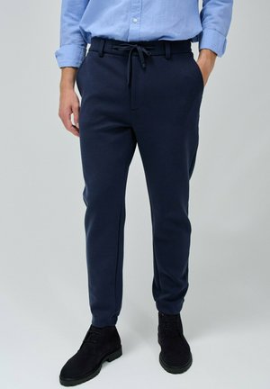 Pantalones de chándal azul marino hechos de una tela suave, con cintura ajustable, pierna estrecha y bolsillos laterales. Combinados con botas negras.