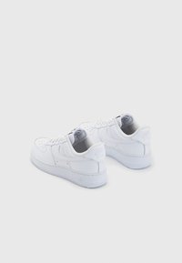 Pair of white Nike Air Force 1 sneakers viewed from the back on a white background, showing laces and sole details.