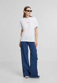 White cotton t-shirt with "Be Kind" in pink, paired with wide-leg blue denim cargo pants featuring visible pockets and frayed hem.