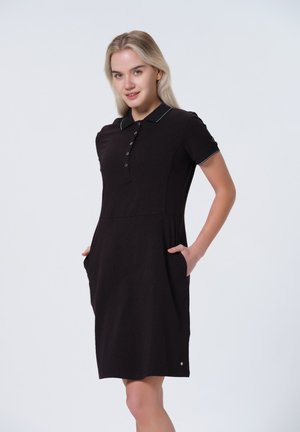 Svart polo-klänning i texturerad tyg med korta ärmar, knapprad, vita detaljer och sidofickor för funktionalitet.