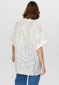 Oversized hvid skjorte med et diskret mønster af grene i lys beige og grå, med en løs pasform og opsmøgede korte ærmer.